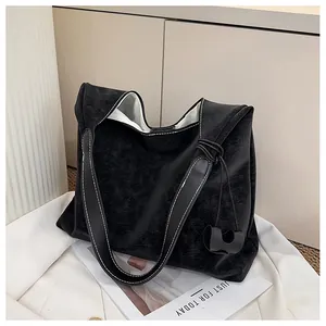 Detail of black suede tote bag featuring white contrast stitching and a side knot charm
