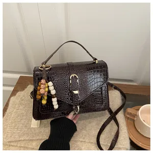 Detail of dark brown crocodile embossed crossbody bag with vintage gold clasp and wood beads