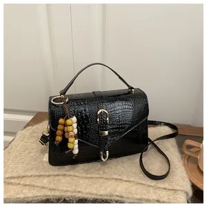 Detail of black crocodile pattern crossbody bag with golden buckle and colorful bead charm