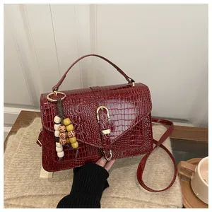 Detail of burgundy crocodile-embossed handbag with beaded tassel and gold buckle