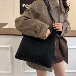 Vintage black tote bag with matte leather texture worn over a brown tweed coat