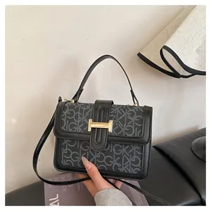 Close-up of a stylish grey monogram small square bag with black leather trim and gold buckle