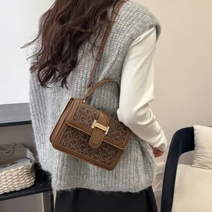 Brown vintage faux leather crossbody bag with logo pattern and gold buckle on a model