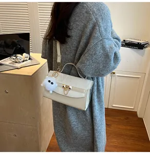 Gros plan du sac crème avec fermoir en V métallique et pendentif en peluche