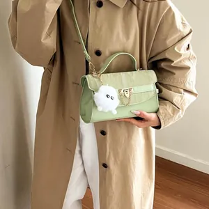 Sac à main cuir vert menthe minimaliste avec chaîne dorée et pompon porté sur manteau