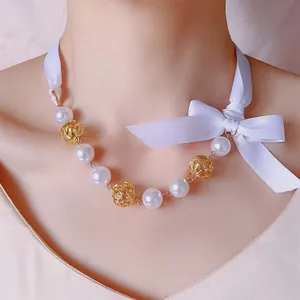 Elegante Perlenkette mit goldenen Hohlkugeln und einer weißen Seidenschleife