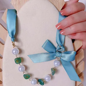 Handgefertigte Kette mit blauem Seidenband, weißen Perlen und grünem Rohstein am Model