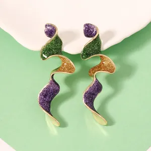 Vue détaillée de boucles d'oreilles ondulées dorées avec émail scintillant violet, vert et orange