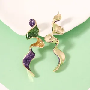 Détail de boucles d'oreilles vagues asymétriques avec émail pailleté et fini doré