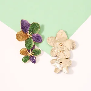 Nahaufnahme von dreifachen Blumenohrringen mit lila-grünem Glitzer und Goldrand