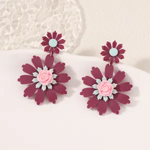 Deep rose and blue sunflower drop earrings made of matte resin on a white display stand
