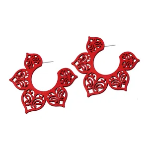Détail de boucles d'oreilles rouges en bois ajouré avec motifs floraux complexes en C