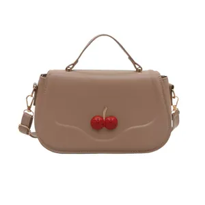 Schicke khakifarbene Handtasche aus Leder mit Kirschanhänger und goldenem Schultergurt