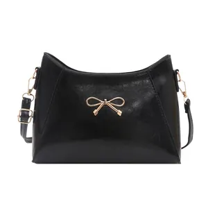 Elegant black glossy shoulder bag with golden bow hardware and slim leather strap