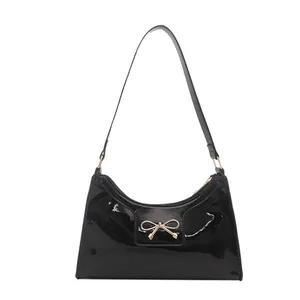 Glossy black patent leather crescent shoulder bag with golden bow buckle detail