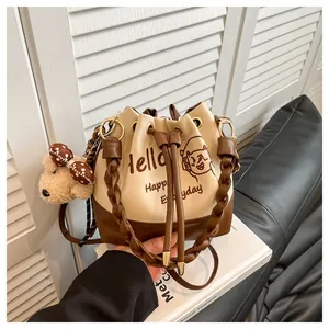 Detail of drawstring bucket bag with letter print, plush bear charm and woven handle