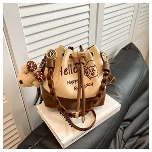 Detail of drawstring bucket bag with hello embroidery and plush bear charm pendant