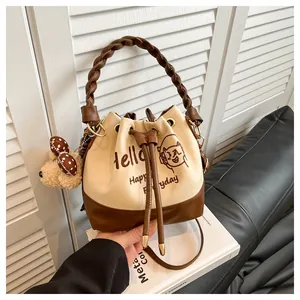 Detail of suede bucket bag with drawstring, woven handle, and teddy bear charm