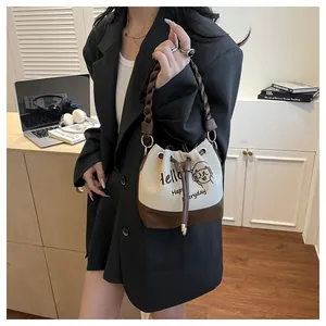 Detail view of large faux suede bucket bag with letter print and woven leather handle