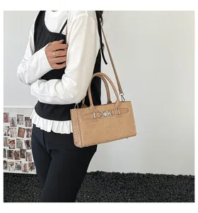 Detail of light beige crocodile textured handbag with a heart-shaped metal buckle accent