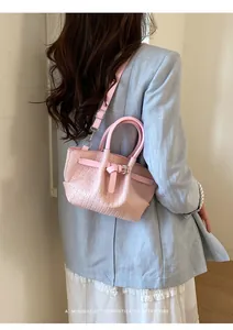 Detail of pink woven handbag with shoulder strap on a model wearing a light blue suit