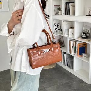 Caramel crocodile pattern handbag with heart buckle shown on model in a modern room