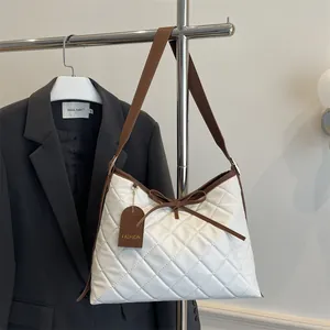 White quilted tote bag with brown straps and bow detail displayed on a dark background
