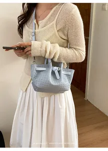 Close-up of light blue woven bucket bag featuring a knotted handle and silver metal charms