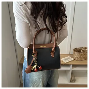 Détail du sac bandoulière en cuir noir avec poignée marron et breloque cerise