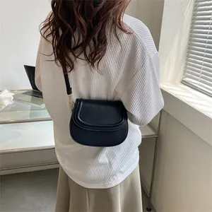 Minimalist black saddle shoulder bag for women with a sleek flap closure and metal hooks