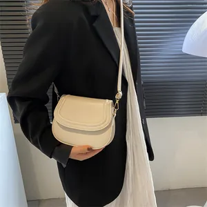 Minimalist beige saddle crossbody bag shown on model with chic black blazer and skirt