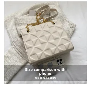 Compact beige crossbody bag with 3D geometric texture next to a smartphone for scale