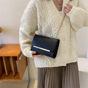 Sac bandoulière minimaliste en cuir noir avec chaîne dorée et barre en métal sur le rabat