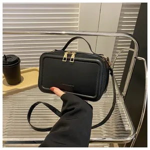 Detail view of black matte leather handbag with gold zippers and adjustable shoulder strap