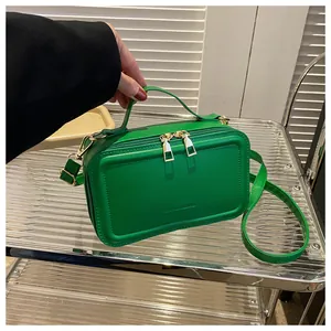 Detail view of green rectangular box bag with golden double zippers and fashion text