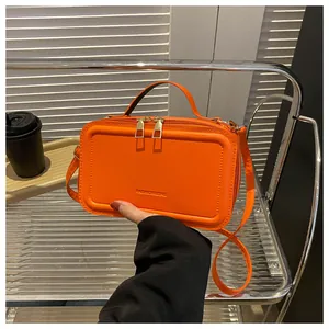 Detail of orange faux leather crossbody bag with dual golden zippers and handle