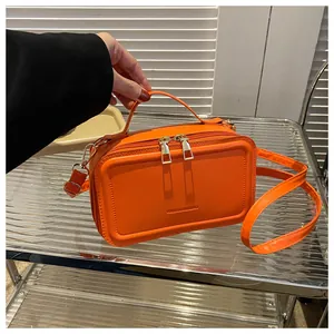 Detail view of bright orange leather handbag featuring dual metal zippers and embossed logo