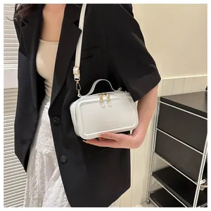 Close-up of white minimalist PU leather crossbody bag with gold zippers on model