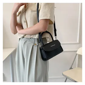 Close-up of a black leather crossbody bag with white text detail and adjustable strap