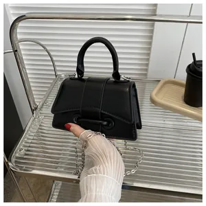 Détail d'un mini sac à main trapèze noir en cuir avec chaîne sur un chariot en verre
