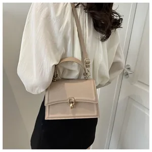Close-up of a beige crossbody bag with gold buckle on a stylish woman outfit