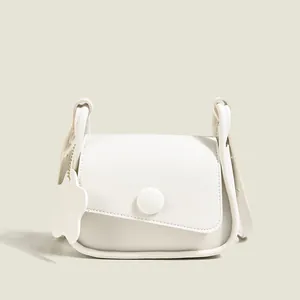 Minimalist white crossbody bag with round buckle detail and floral charm accessory