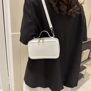 White leather crossbody bag with gold zippers and detachable strap worn by model