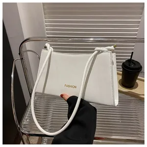 Détail d'un sac baguette en cuir blanc avec texte FASHION doré et bandoulière fine
