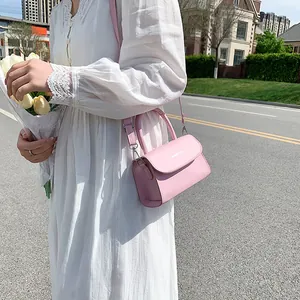 Pink faux leather crossbody bag with top handle and magnetic flap closure in sunlight