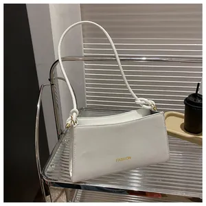 Détail du sac baguette en cuir blanc avec texte Fashion doré et nœud sur l'anse