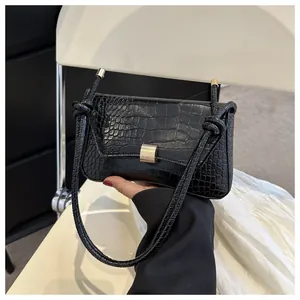 Détail du sac baguette noir motif crocodile avec boucle dorée et détail de nœud