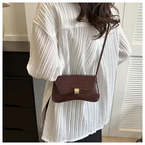 Détail d'un sac bandoulière marron foncé effet croco porté avec une chemise plissée