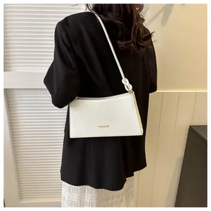 Détail du sac baguette blanc avec texte FASHION doré et bandoulière à nœud au bras