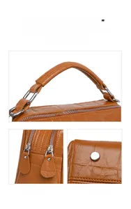 Detail view of brown crocodile texture, dual zippers, and bottom metal studs of the handbag